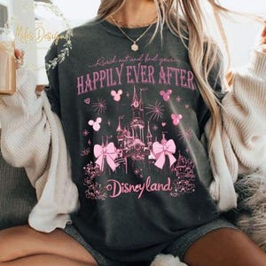 May include: A dark gray sweatshirt with a pink graphic of Cinderella's castle, Mickey Mouse ears, and the text "Reach out and find your happily ever after Disneyland".