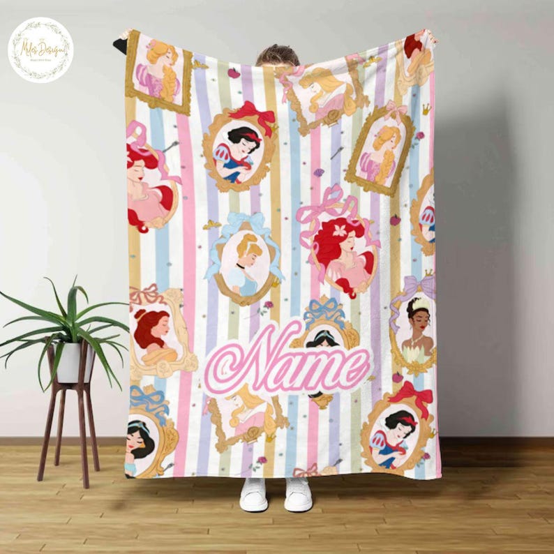 May include: A colorful blanket featuring framed illustrations of Disney princesses on a striped background. The blanket has a pink, blue, and yellow color scheme, with the word "Name" in a cursive font.