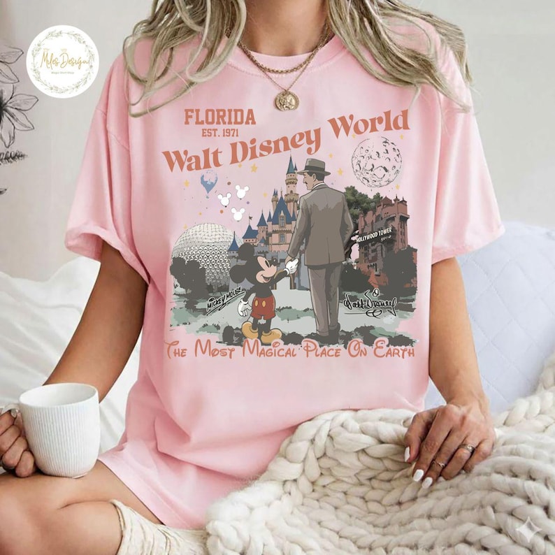 Puede incluir: Camiseta rosa claro con un dise&ntilde;o de Walt Disney World en Florida. El dise&ntilde;o incluye a Mickey Mouse, un hombre y varios puntos de referencia del parque. El texto en la camiseta dice "Florida, Walt Disney World, The Most Magical Place On Earth."