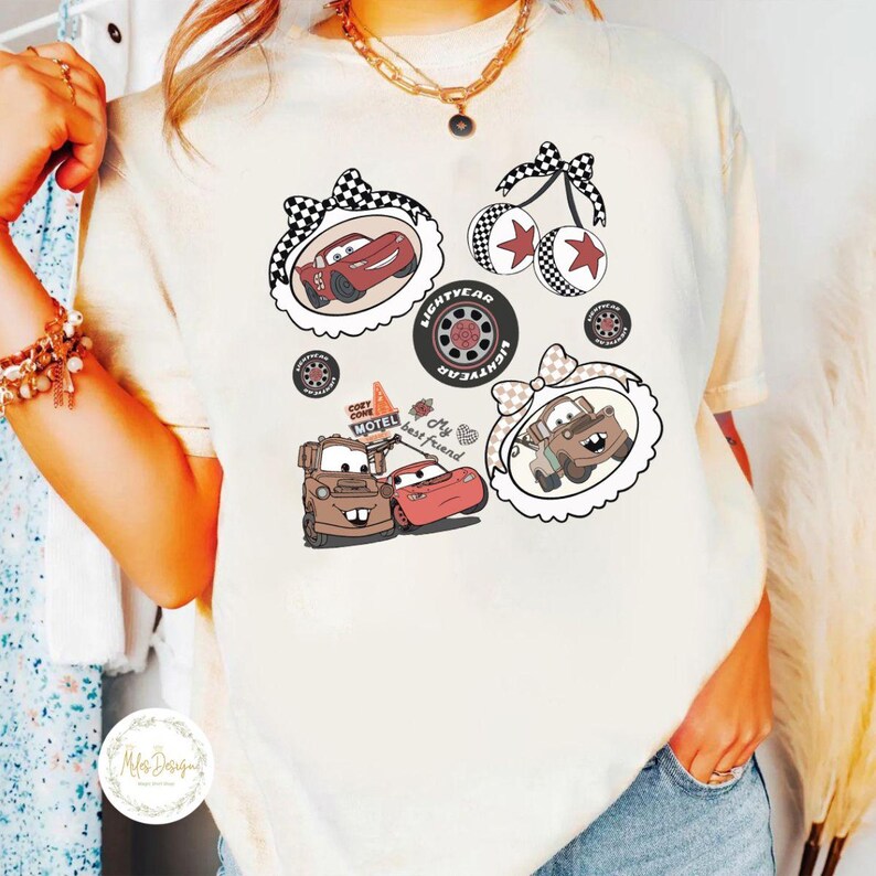 K&ouml;nnte beinhalten: Cremefarbenes T-Shirt mit Cartoon-Autografiken. Designs umfassen Rennwagen, Kirschen und einen Reifen mit dem Wort "Lightyear". Das Shirt hat eine lockere Passform und einen Rundhalsausschnitt.