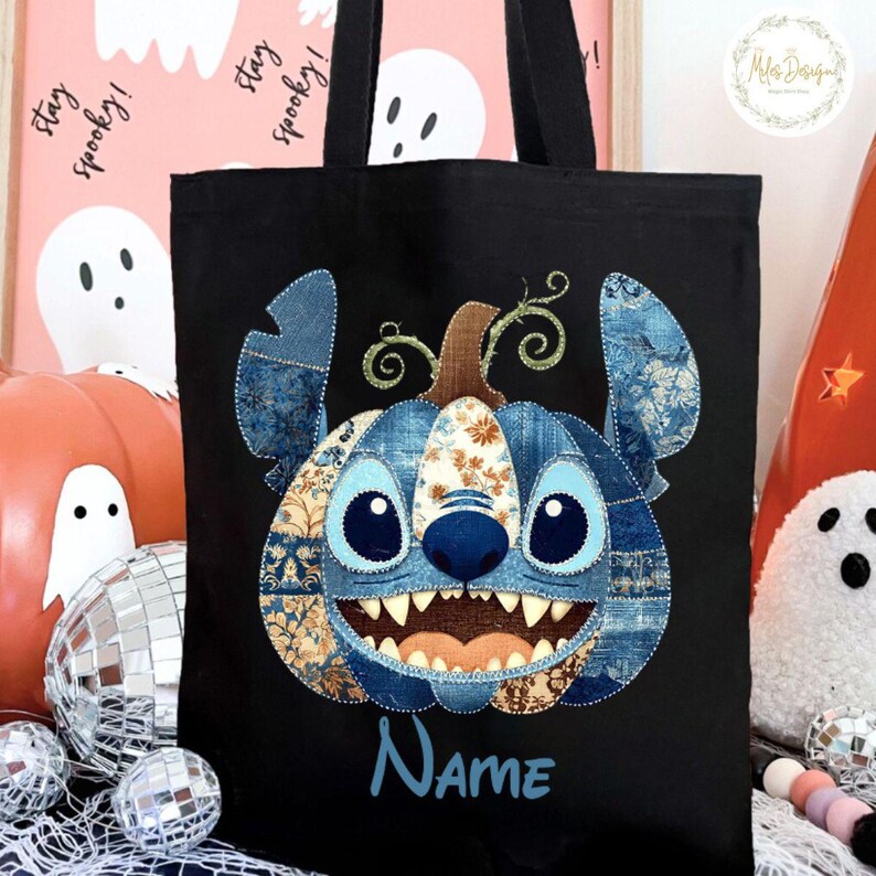 Pode incluir: Saco tote preto com um design de ab&oacute;bora patchwork azul e bege, semelhante ao Stitch. A palavra "Name" &eacute; bordada em azul. O saco tem al&ccedil;as pretas, ideal para o Halloween.