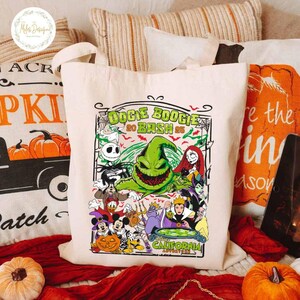 May include: A cream-colored tote bag featuring a colorful graphic for the Oogie Boogie Bash 2025 event. The design includes various Disney characters and the text "Oogie Boogie Bash 2025" in green. The bag has two handles.