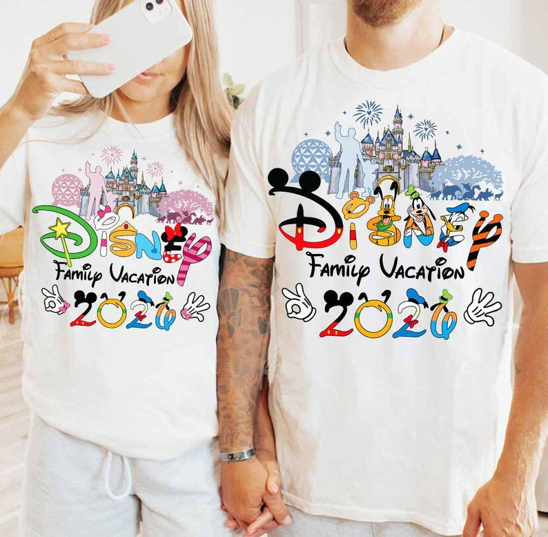 May include: Two white t-shirts with a colorful Disney Family Vacation 2020 design. The design includes Disney characters, a castle, fireworks, and the Disney logo. The shirts are short-sleeved.