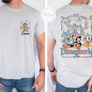 Pu&ograve; includere: Due magliette grigie a tema Disney World. La maglietta anteriore ha un'immagine di cartone animato di Pluto e il testo "James". La maglietta posteriore ha un'immagine di cartone animato di Topolino, Minnie Mouse, Paperino, Pippo e Pluto davanti al Castello di Cenerentola con il testo "Disneyworld Est. 1971".