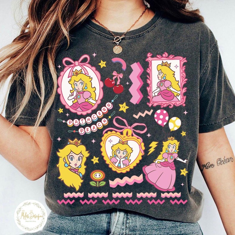 May include: Dark gray t-shirt featuring Princess Peach graphics in pink, yellow, and white. The design includes various Princess Peach portraits, stars, cherries, and the text "Princess Peach". The shirt has a vintage, washed look.