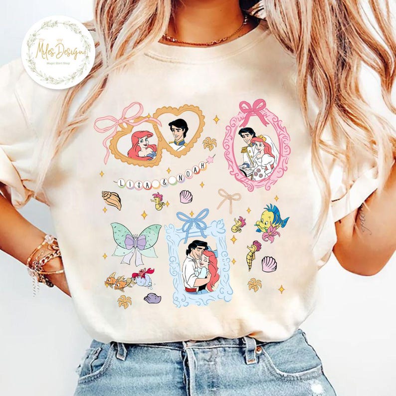Puede incluir: Una camiseta blanca con un dise&ntilde;o colorido que presenta a Ariel y al Pr&iacute;ncipe Eric de La Sirenita. El dise&ntilde;o incluye corazones, conchas marinas y una pancarta que dice "Ariel & Noah".