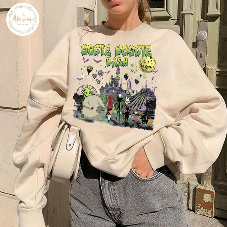 May include: Beige sweatshirt with a colorful graphic featuring the text "Oogie Boogie Bash" and various Halloween-themed characters and elements. The design includes a castle, a full moon, and other spooky details.