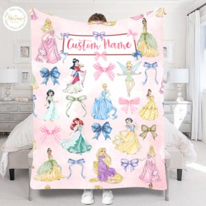 May include: A pink blanket featuring illustrations of various princesses and bows. The blanket has the text "Custom Name" in a decorative font. The princesses are depicted in their signature gowns, with a watercolor effect.