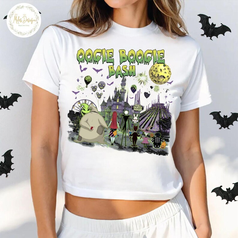 May include: White t-shirt featuring a colorful graphic design with the text "Oogie Boogie Bash". The design includes characters and elements from a Halloween-themed movie, with a haunted house and a full moon. Black bats are scattered around the shirt.
