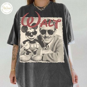 May include: Charcoal grey t-shirt with a retro graphic of Mickey Mouse in sunglasses and Walt Disney, with the name "Walt" in red script. The design has a distressed, aged appearance, giving it a vintage feel.
