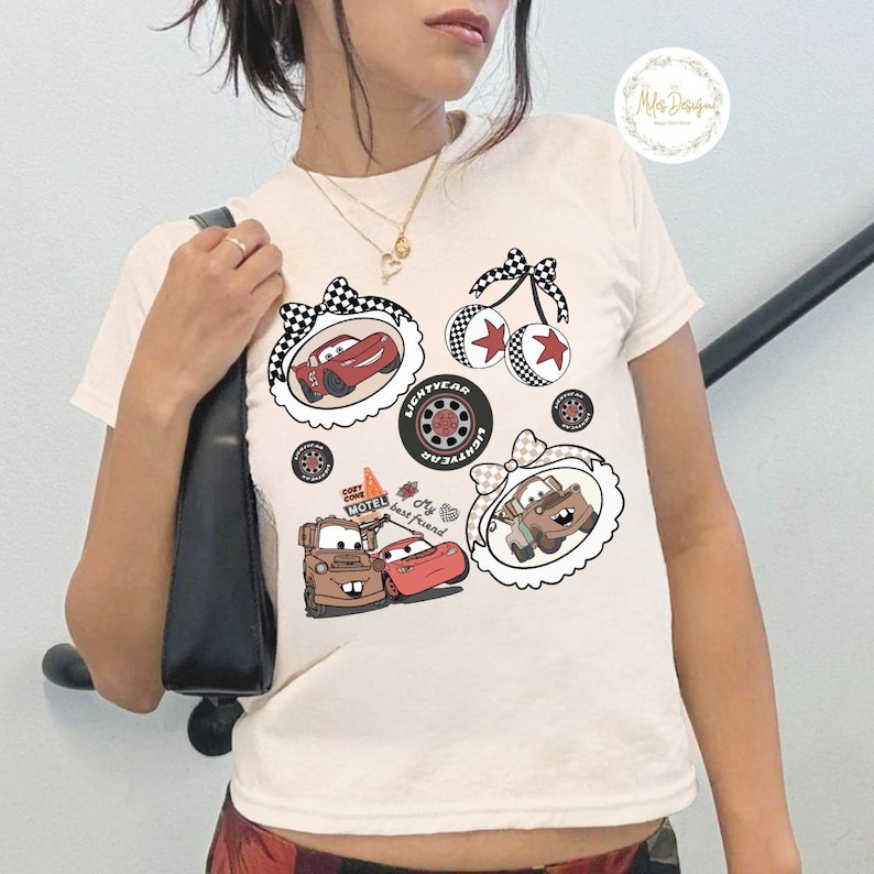 K&ouml;nnte beinhalten: Cremefarbenes T-Shirt mit Cartoon-Bildern von Charakteren aus dem Film Cars. Die Grafiken zeigen Lightning McQueen, Hook und andere Elemente, umrahmt von dekorativen Bord&uuml;ren und Schleifen. Das Shirt hat auch den Text "My best friend".