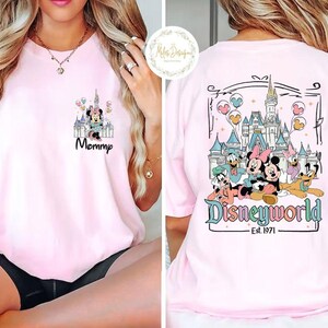 Pu&ograve; includere: Maglietta rosa con una grafica di Topolino e i suoi amici davanti al Castello di Cenerentola. Il testo "Disneyworld Est. 1971" &egrave; stampato sotto la grafica. La parte anteriore della maglietta ha una grafica pi&ugrave; piccola di Minnie Mouse davanti al Castello di Cenerentola con il testo "Mommy".