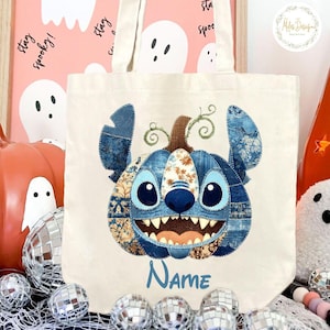 Pode incluir: Bolsa tote de lona creme com um design de personagem azul em forma de ab&oacute;bora. O personagem tem olhos grandes, um sorriso largo e detalhes de patchwork de ganga. A palavra "Name" est&aacute; escrita em azul abaixo.
