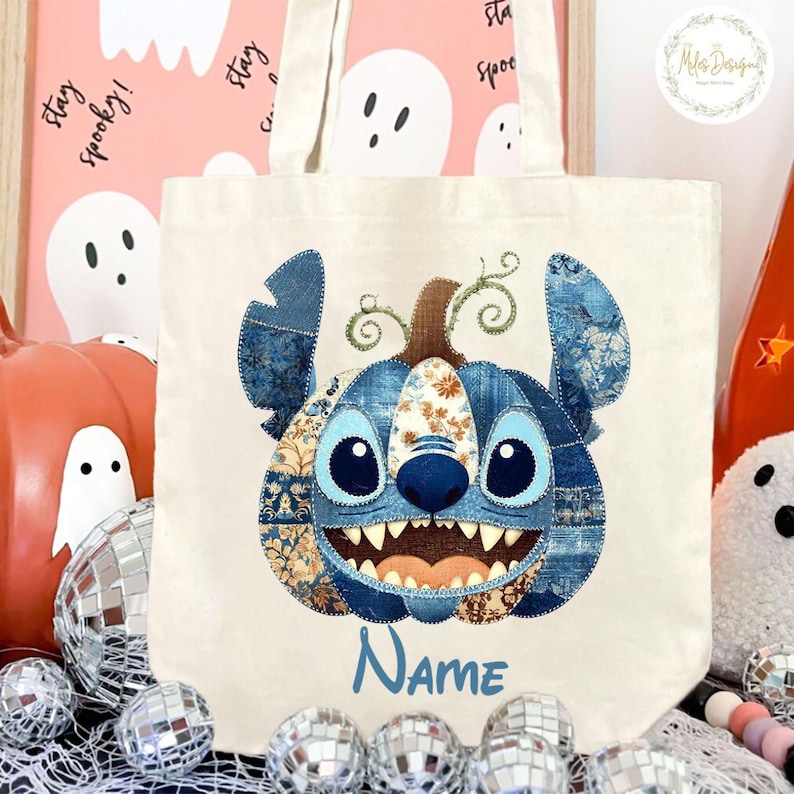 Pode incluir: Bolsa tote de lona creme com um design de personagem azul em forma de ab&oacute;bora. O personagem tem olhos grandes, um sorriso largo e detalhes de patchwork de ganga. A palavra "Name" est&aacute; escrita em azul abaixo.