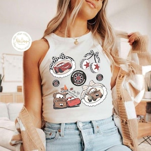 K&ouml;nnte beinhalten: Cremefarbenes Tanktop mit Cartoon-Autografiken. Designs umfassen ein rotes Rennauto, Kirschen, einen Reifen und die Charaktere Mater und Lightning McQueen. Das Tanktop hat einen runden Ausschnitt und ist &auml;rmellos.