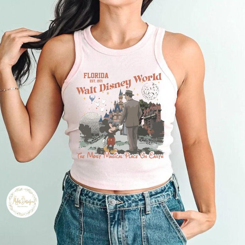 Puede incluir: Una camiseta sin mangas rosa claro con un gr&aacute;fico de Walt Disney World. El gr&aacute;fico incluye a Mickey Mouse, un hombre con traje, un castillo y el texto "Florida Walt Disney World The Most Magical Place On Earth".