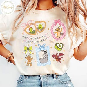 Op de afbeelding: Een wit T-shirt met een grafische print van personages uit de film Shrek. De grafiek bevat Shrek, Fiona, Ezel, Puss in Boots en een gingerbread man. De tekst "Can't today I'm swamped" is op het shirt gedrukt.