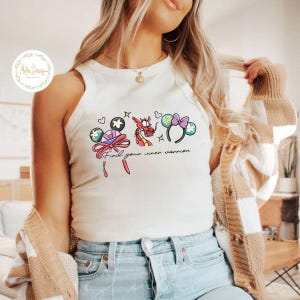 May include: White tank top with a colorful graphic featuring cartoon character ears, a dragon, and the text "Find your inner warrior." The design includes pink, blue, and black accents.
