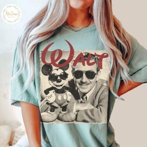 May include: A pale blue t-shirt with a retro graphic of Mickey Mouse in sunglasses alongside Walt Disney, with the name "Walt" in red. The design is printed on a soft, comfortable t-shirt.