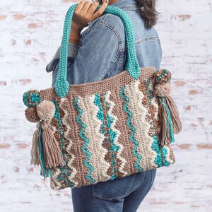 May include: A crocheted tote bag with a chevron pattern in brown, beige, and turquoise. The bag has pom-poms and tassels in brown and turquoise.
