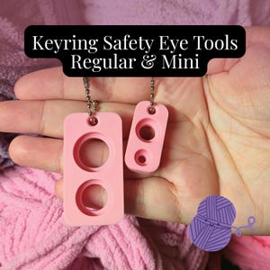 May include: Two light pink rectangular safety eye tools, one regular and one mini size, each featuring circular cutouts and attached to a silver metal ball chain. The text Keyring Safety Eye Tools Regular & Mini is displayed above the tools.