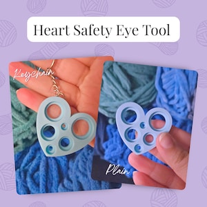May include: A light blue heart-shaped safety eye tool with multiple circular cutouts of varying sizes. The tool is shown in two versions: one attached to a metal keychain and one plain version without the keychain attachment.