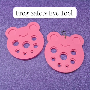 May include: Two pink Frog Safety Eye Tools with a frog-shaped design featuring multiple circular cutouts of varying sizes. One tool includes a small metal ball chain attached to the top. The text Frog Safety Eye Tool is printed above them.