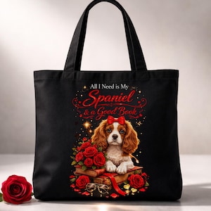 May include: Black tote bag featuring a Cavalier King Charles Spaniel with a red bow, surrounded by red roses and books. The text reads "All I Need is My Spaniel & a Good Book". A single red rose is on the left.