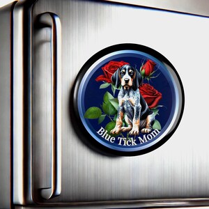 May include: A round magnet with a blue background and a black border. A blue tick hound puppy sits in the center of the magnet, surrounded by red roses. The text "Blue Tick Mom" is written in a white arc below the puppy.