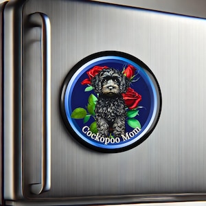 May include: A round magnet with a blue border and a black and white Cockapoo puppy standing in front of red roses. The text "Cockapoo Mom" is written on the magnet.