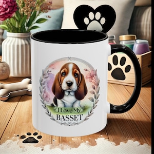 May include: White ceramic coffee mug with a black rim and handle. The mug features a colorful illustration of a Basset Hound puppy with the text "I Love My BASSET" on the front.