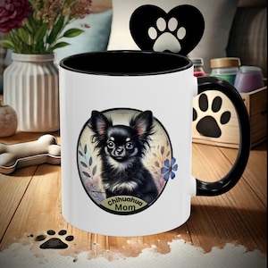 Op de afbeelding: Witte keramische koffiemok met een zwarte rand en handvat. De mok heeft een illustratie van een zwart-witte chihuahua met de tekst "Chihuahua Mom" in een gouden cirkel.