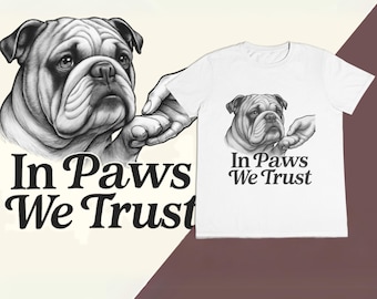 Puede incluir: Una camiseta blanca con una ilustración en blanco y negro de un bulldog dando la pata a una mano. El texto "In Paws We Trust" está impreso debajo de la imagen.
