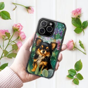 Peut inclure: Une coque de smartphone transparente avec une illustration graphique d'un chiot Chihuahua à poils longs noir et feu assis parmi des feuilles vertes et des fleurs colorées. La coque présente une découpe pour l'objectif photo en haut à gauche.