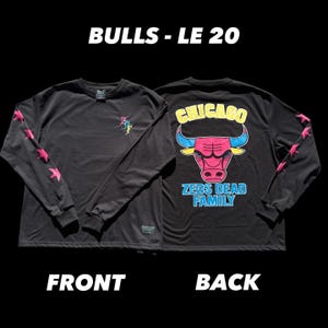 May include: Black long-sleeve shirt with the text "BULLS - LE 20" at the top. The front of the shirt has a small graphic, and the sleeves have pink star designs. The back features a Chicago Bulls logo and the text "ZEDS DEAD FAMILY".