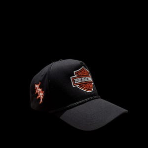 Könnte beinhalten: Schwarze Baseballkappe mit gebogenem Schirm. Auf der Kappe befindet sich ein gesticktes orange-weißes Logo mit der Aufschrift "Zeds Dead Family". Auf der Seite befindet sich ein orangefarbenes Design.