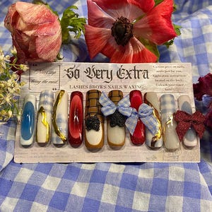 May include: A set of custom press-on nails with various designs, including blue, gold, red, and plaid patterns. Some nails feature bows and textured accents. The card reads "So Very Extra" and "Lashes Brows Nails Waxing."