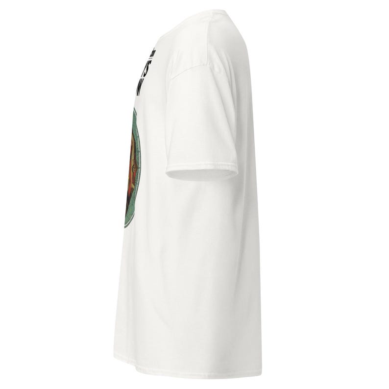 May include: White t-shirt with a circular graphic on the front. The graphic features a portrait with a green border and text above. The shirt has short sleeves and a crew neck.