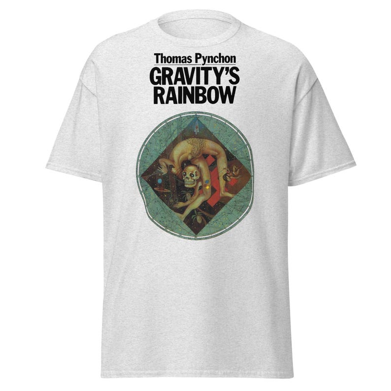 May include: Light gray t-shirt featuring the text "Thomas Pynchon GRAVITY'S RAINBOW" in black. Below the text is a circular graphic with a figure in a contorted pose, with a skull and other figures in a diamond shape.