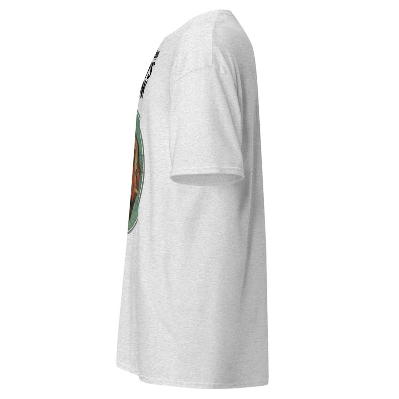 May include: A light gray t-shirt with a circular graphic on the front. The graphic features a brown image within a green circle, with black text above. The shirt has short sleeves and a crew neck.