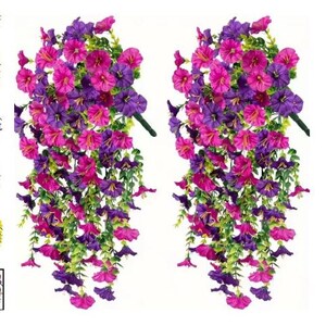 以下が含まれることがあります： ピンクと紫の花がついた、2つの吊り下げ式の人工花アレンジメント。花は緑色の茎から下に流れ落ちています。