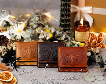 May include: Three leather wallets in sand, dark brown, and leather colors, each with a floral design. The wallets are displayed with text labels and are personalized with names. The wallets are rectangular and have a textured surface.