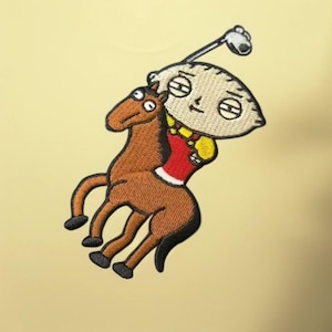 May include: An embroidered patch featuring a cartoon character with a large oval head and a golf club, riding a brown horse. The character wears a red shirt with yellow accents. The design is rendered in detailed thread work with black outlines.