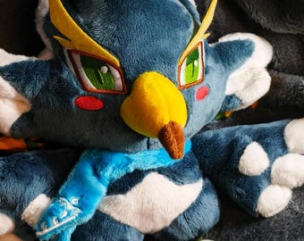 May include: A plush bird toy with a blue body, white accents, and yellow details. The toy has green eyes, a yellow beak, and a blue scarf. The feet are green and white. The toy is made of soft, plush material.