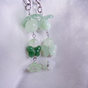 May include: A silver chain with green and white jade beads, butterfly charms, and flower charms.