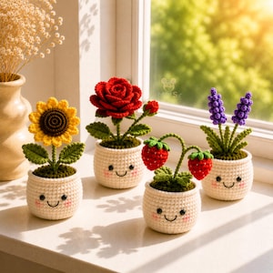 Pode incluir: Quatro plantas em vaso de crochê, incluindo um girassol amarelo, uma rosa vermelha, dois morangos vermelhos e lavanda roxa. Cada planta está num pequeno vaso de crochê cor de creme com um rosto sorridente bordado, olhos pretos e bochechas rosadas.