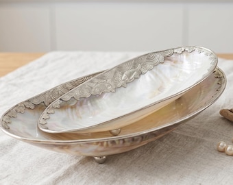 May include: Two oval serving dishes. The larger dish is silver-toned with three small feet. The smaller dish sits inside the larger one. Both dishes have a mother-of-pearl interior and a decorative silver-toned border.