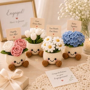 May include: Four crocheted potted plants with smiling faces, each holding a sign. The signs read: Happily Ever After, Love Grows Here, Two Hearts One Home, and Better Together. The plants feature white and pink roses, white tulips, daisies, and blue flowers.