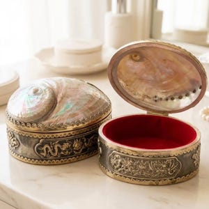May include: Two decorative jewelry boxes. One is closed, the other open. Both have a silver and gold-toned metal base with a dragon design. The lids are made of a pearlescent shell material, and the open box has a red velvet interior.