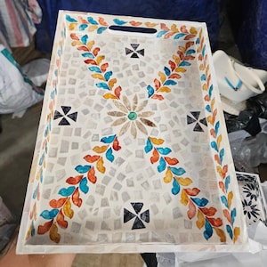 May include: Rectangular serving tray with a mosaic tile design. The tray has a white background and is decorated with colourful leaf and flower patterns in blue, orange, and yellow. It has cut-out handles.